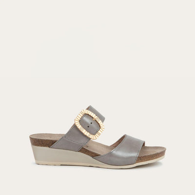 Profile view of a metalic gray slip-on wedge sandal with two straps and a large textured buckle. 