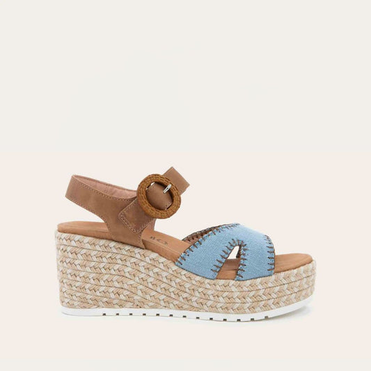Profile view of a blue/brown wedge sandal with a woven platform and brown leather ankle strap, fastened by a circular buckle. 