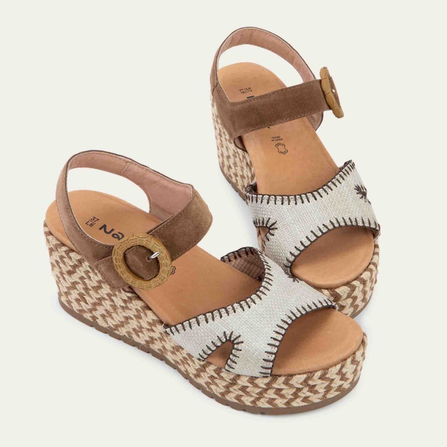 Pair of beige/brown wedge sandals with a woven platform and brown suede ankle strap, fastened by a circular buckle. 