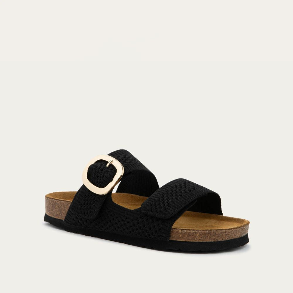 Angled profile view of a black slip-on sandal with two adjustable knit straps and a large gold buckle. It has a cork footbed and a black sole.