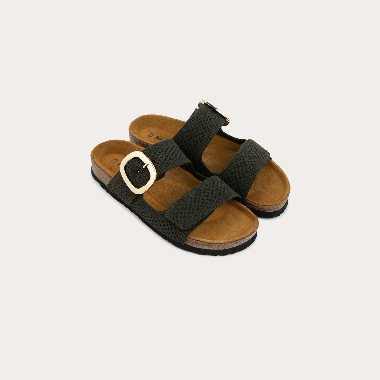Pair of blue slip-on sandals with two adjustable knit straps and a large gold buckle. It has a cork footbed and a black sole.