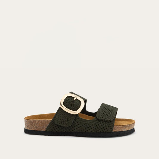 Profile view of a green slip-on sandal with two adjustable knit straps and a large gold buckle. It has a cork footbed and a black sole.