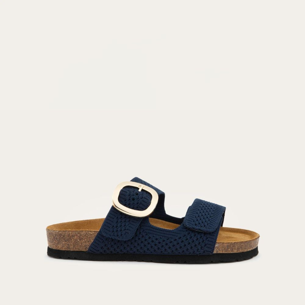 Profile view of a blue slip-on sandal with two adjustable knit straps and a large gold buckle. It has a cork footbed and a black sole.