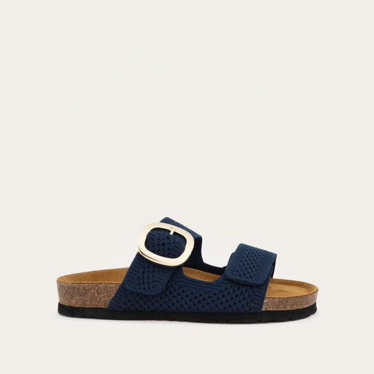 Profile view of a blue slip-on sandal with two adjustable knit straps and a large gold buckle. It has a cork footbed and a black sole.