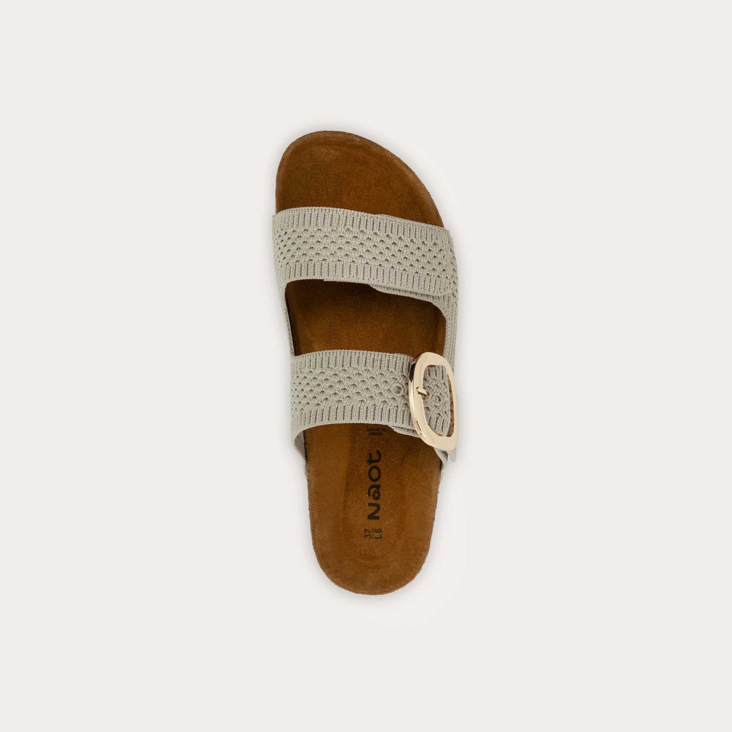 Top view of a beige  slip-on sandal with two adjustable knit straps and a large gold buckle. It has a cork footbed and a black sole.