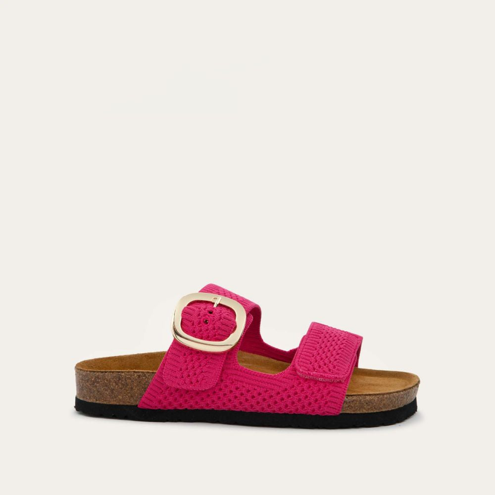 Profile view of a pink slip-on sandal with two adjustable knit straps and a large gold buckle. It has a cork footbed and a black sole.