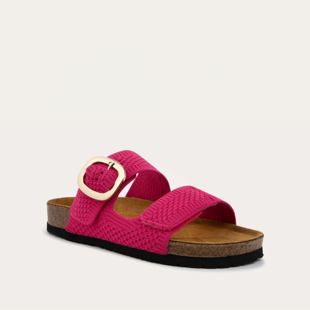 Angled profile view of a pink  slip-on sandal with two adjustable knit straps and a large gold buckle. It has a cork footbed and a black sole.