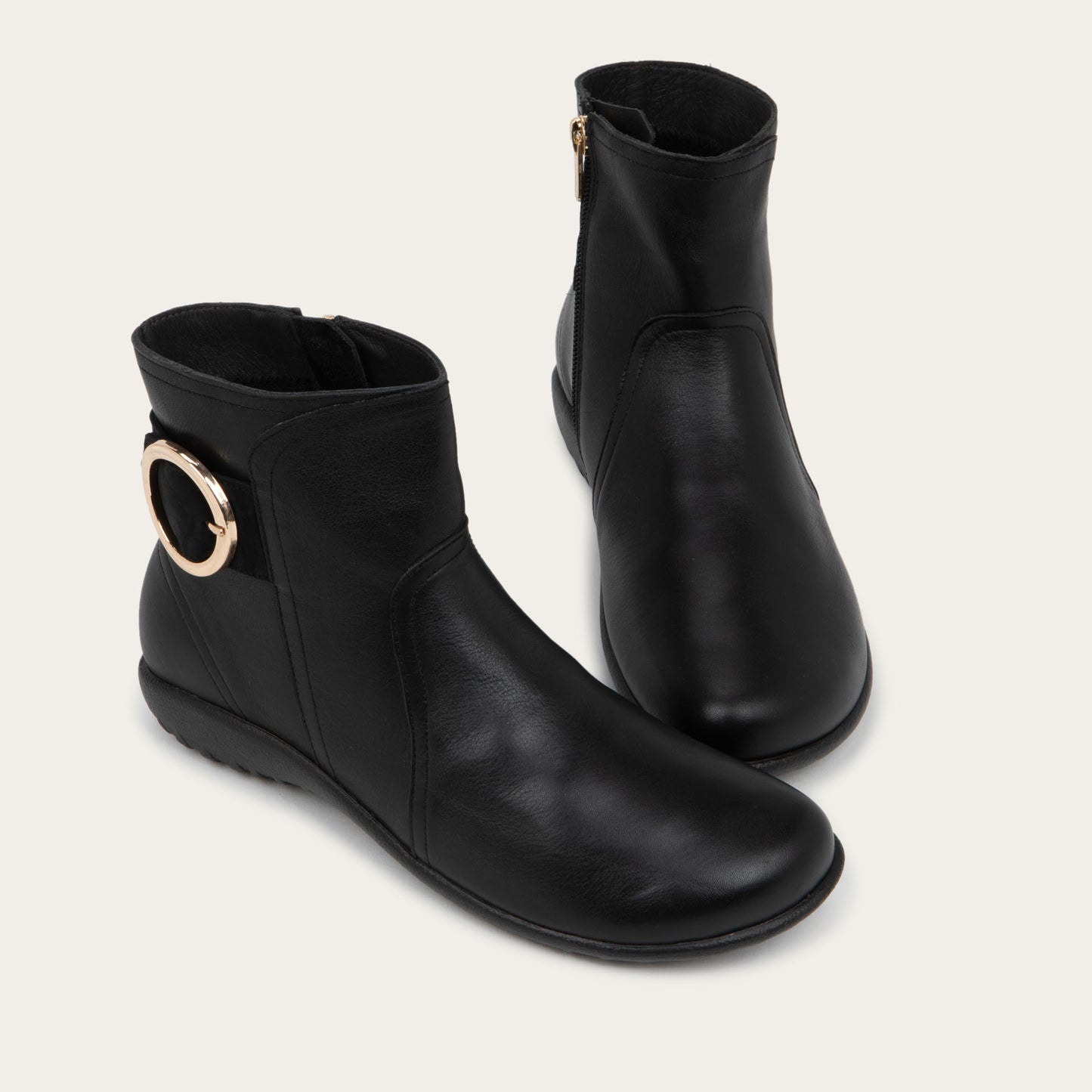 Pair of black boots featuring an accent strap with round buckle in the back of the shoe on a dark sole.