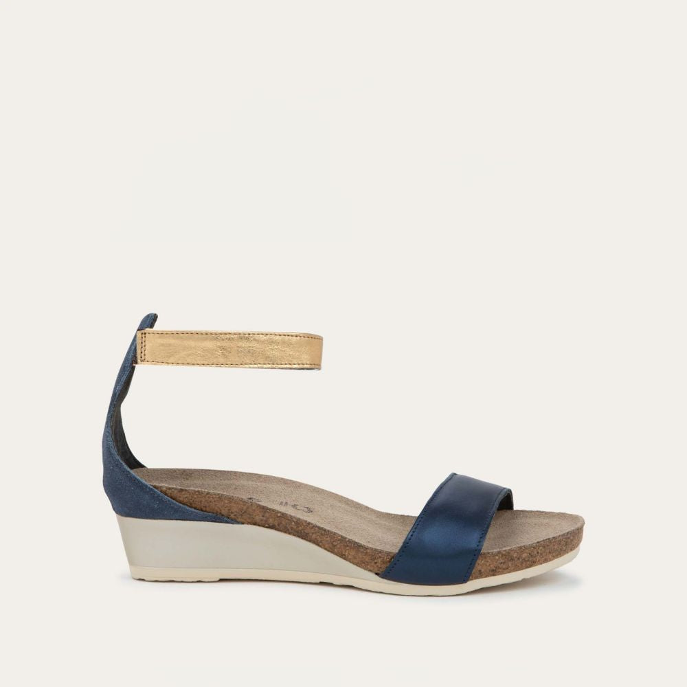 Profile view of a blue wedge sandal with cork sole, featuring an open toe and metallic gold ankle strap.