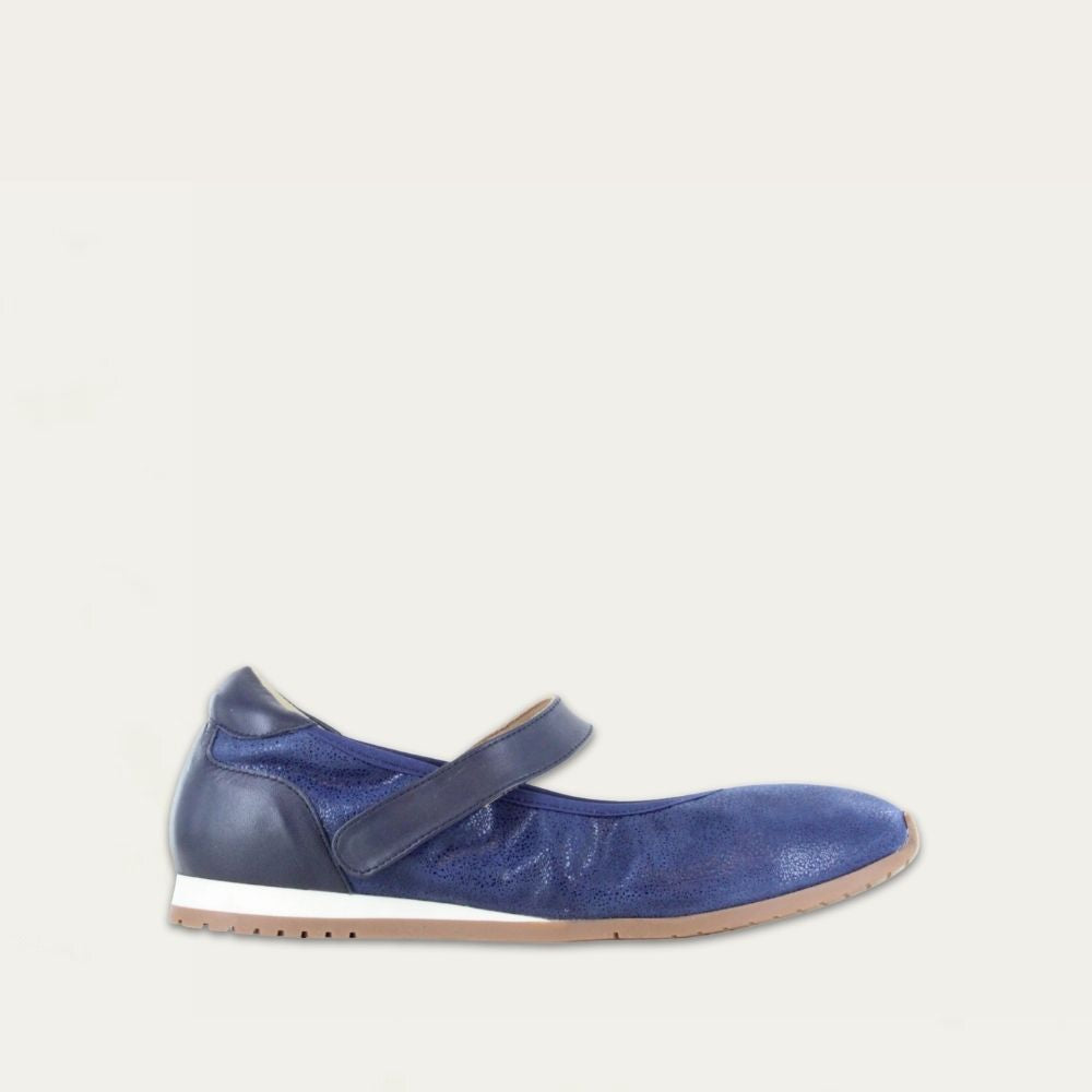 Profile view of a blue suede mary jane featuring leather accents on a low white and beige sole. 