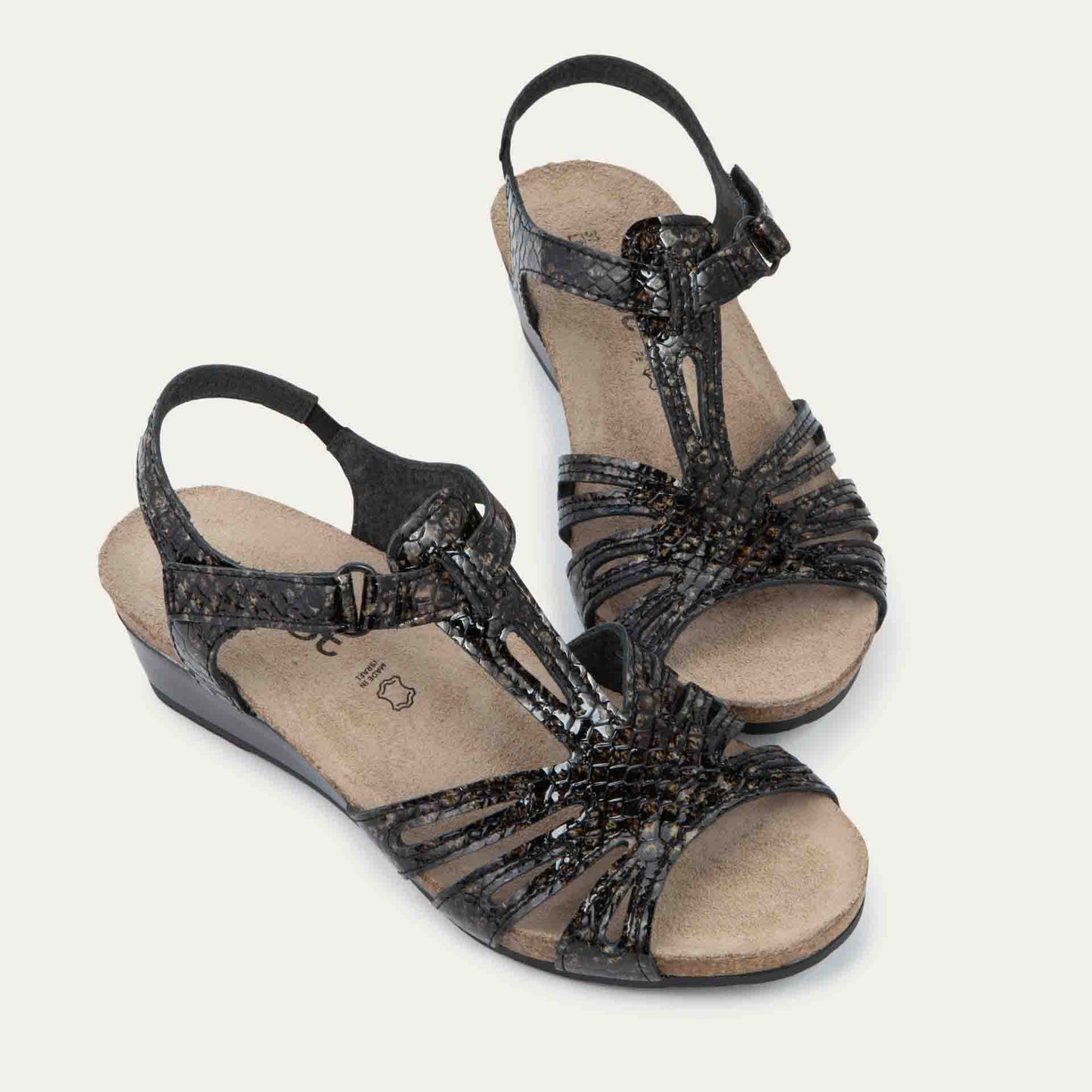 A pair of reptile printed wedge sandals with strappy design, open toe, and adjustable ankle strap on a cork footbed.