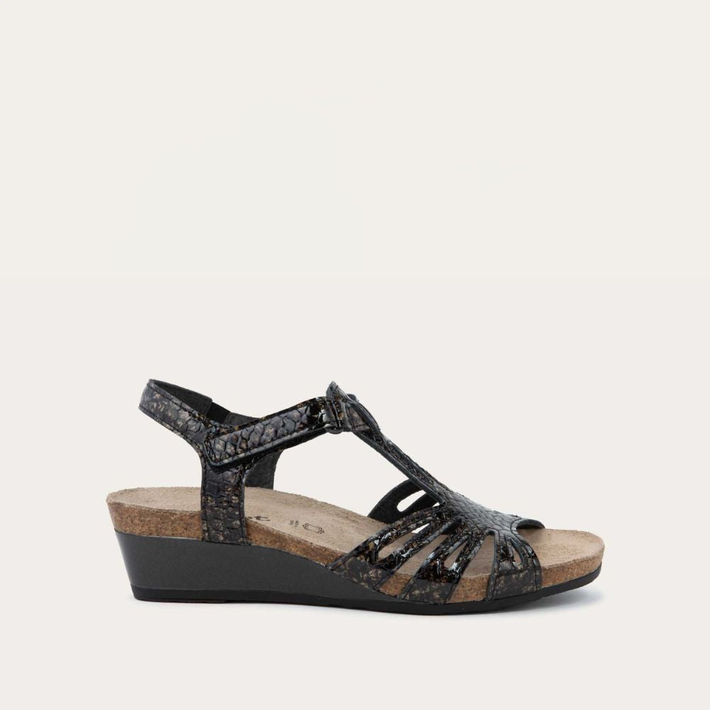 Profile view of a  reptile printed wedge sandal with strappy design, open toe, and adjustable ankle strap on a cork footbed.