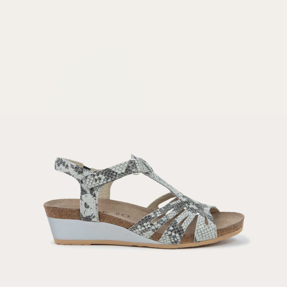Profile view of a  black and white reptile printed wedge sandal with strappy design, open toe, and adjustable ankle strap on a cork footbed.