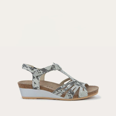 Profile view of a  black and white reptile printed wedge sandal with strappy design, open toe, and adjustable ankle strap on a cork footbed.
