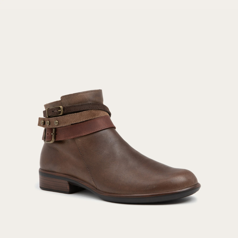 Angled view of a brown leather ankle boot with two decorative straps and brass buckles. The boot has a low heel and a smooth, polished finish, conveying a stylish look.