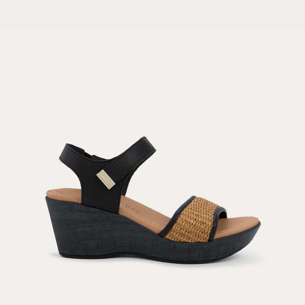 Profile view of a wedge heeled sandal with a black leather ankle strap, and woven tan front strap