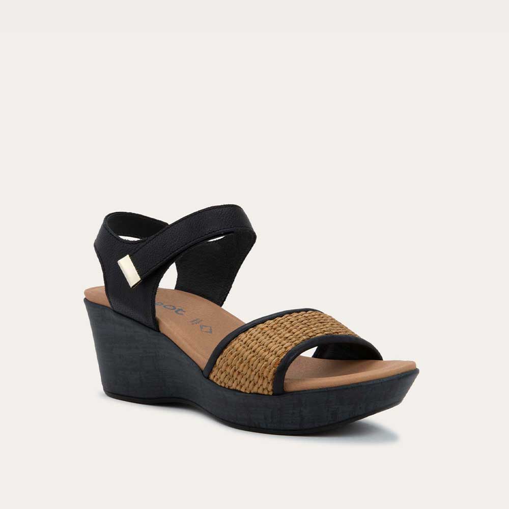 Angled profile view of a wedge heeled sandal with a black leather ankle strap, and woven tan front strap