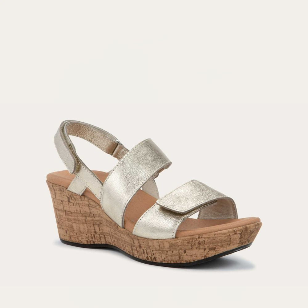 Angled profile view of a gold sandal with metallic straps on a cork wedge sole. Features an open toe and wedge heel.