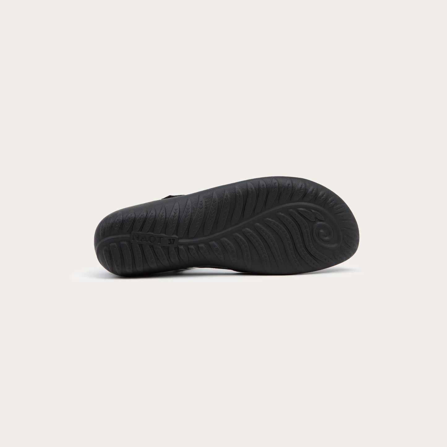 Bottom view of a black Mary Jane featuring contrasting materials and cutouts by the heel on a dark sole.