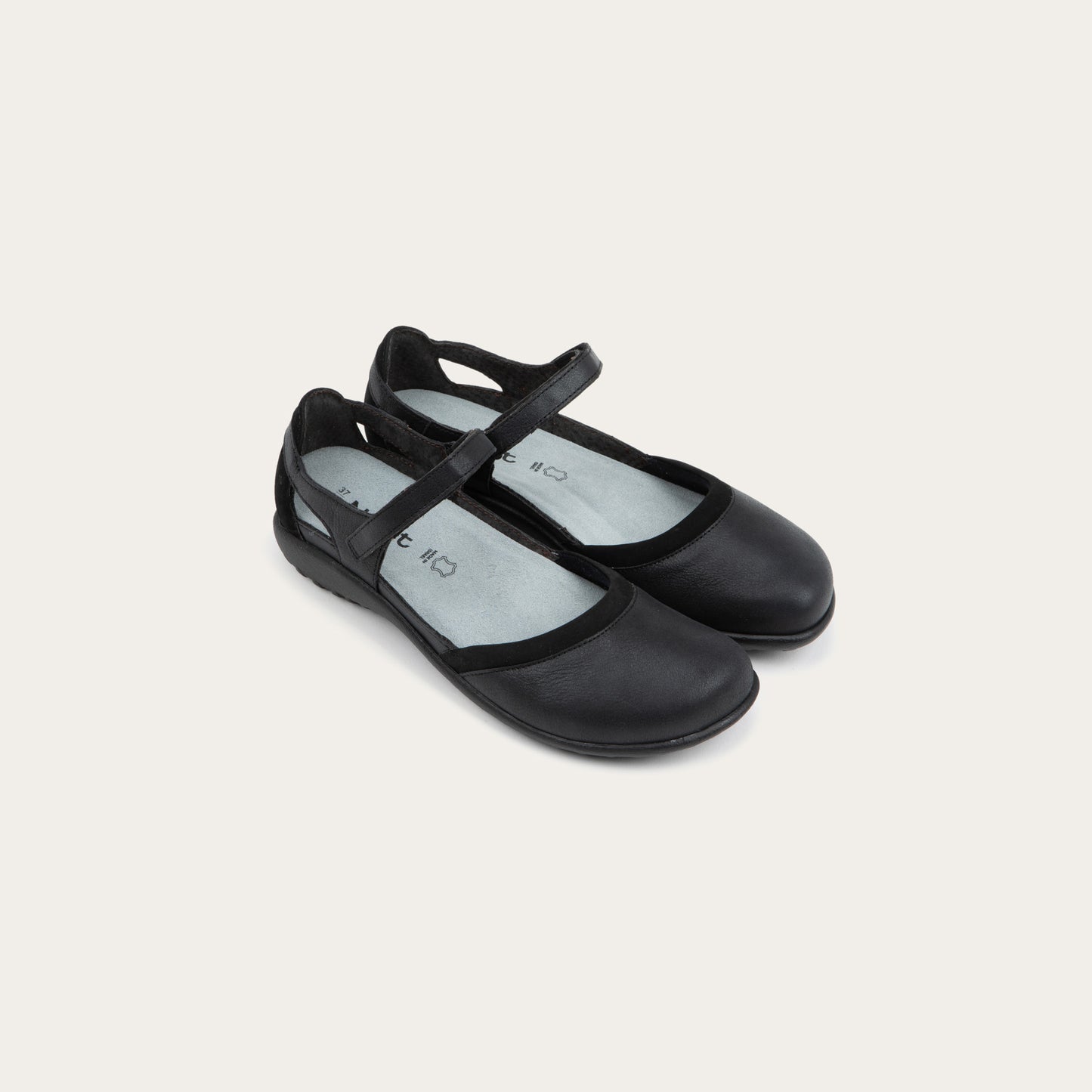 Pair of  black Mary Janes featuring contrasting materials and cutouts by the heel on a dark sole.
