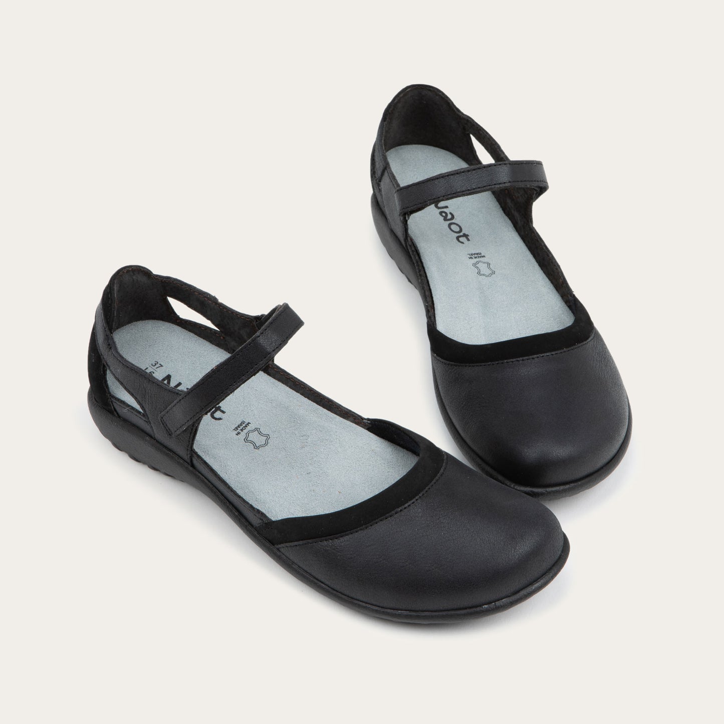 Pair of  black Mary Janes featuring contrasting materials and cutouts by the heel on a dark sole.