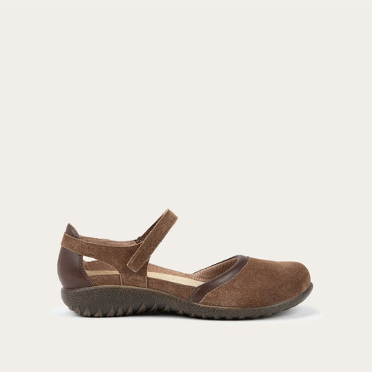 Profile view of a brown Mary Jane featuring contrasting materials and cutouts by the heel on a dark sole.