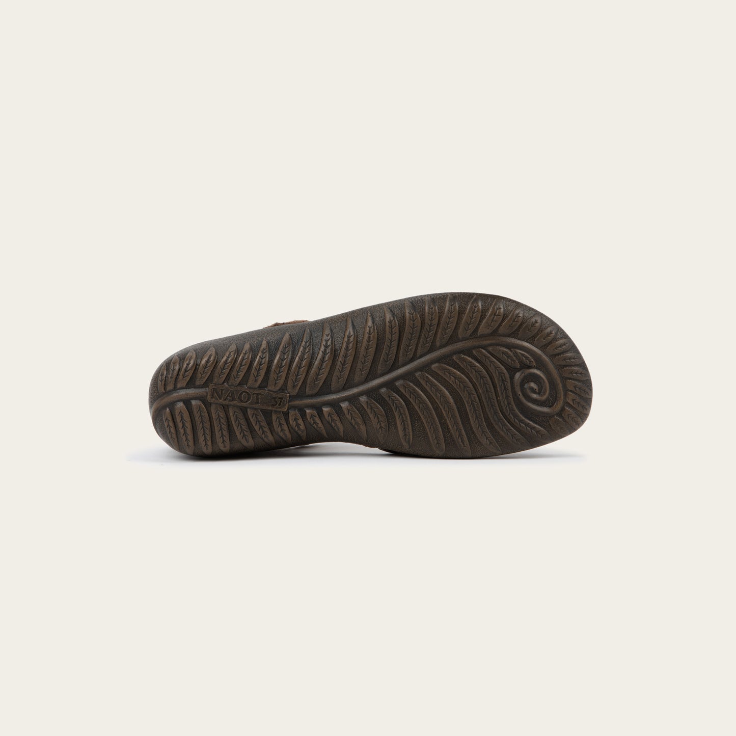 Bottom view of a brown Mary Jane featuring contrasting materials and cutouts by the heel on a dark sole.