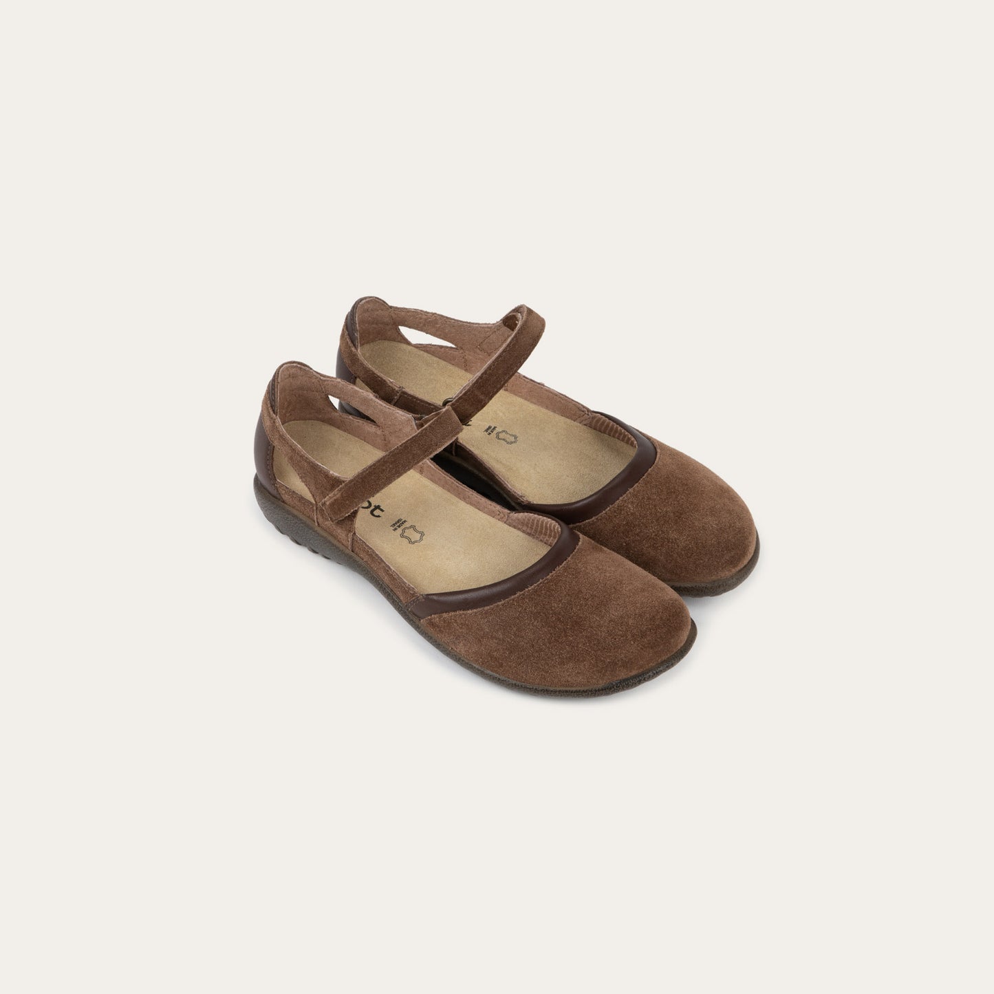 Pair of  brown Mary Janes featuring contrasting materials and cutouts by the heel on a dark sole.