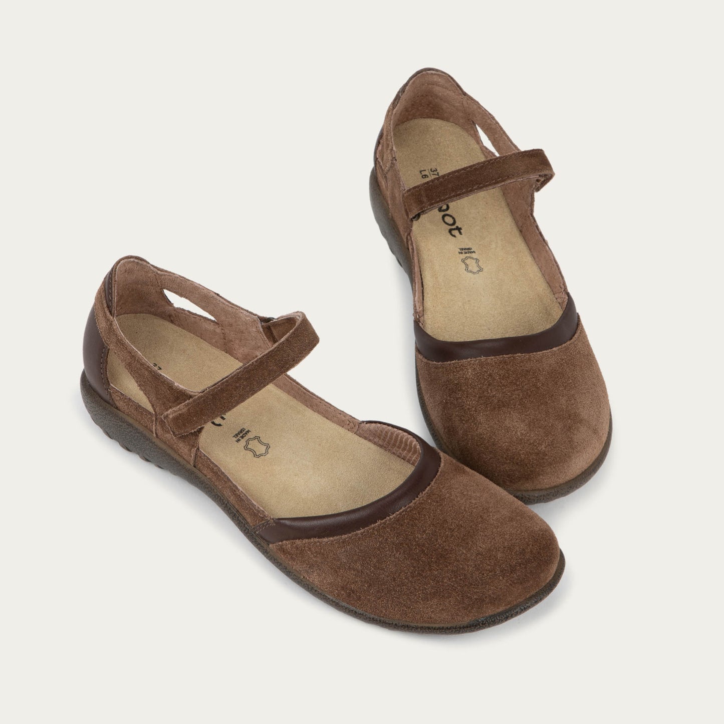 Pair of  brown Mary Janes featuring contrasting materials and cutouts by the heel on a dark sole.