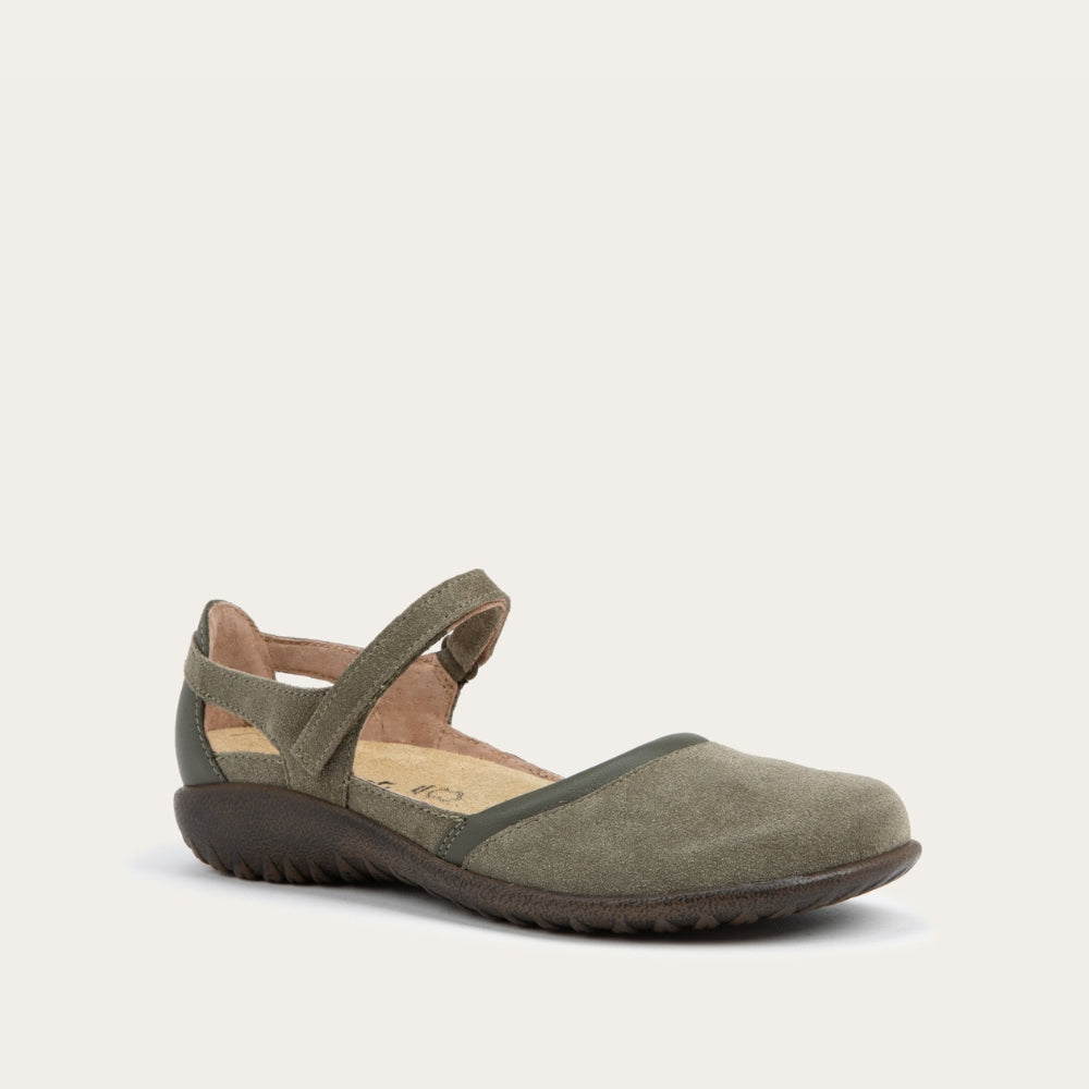 Angled profile view of a green Mary Jane featuring contrasting materials and cutouts by the heel on a dark sole.
