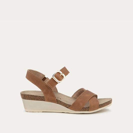 Profile view of a cork footbed,  brown wedge sandal with cross straps and a gold buckle on the ankle strap. 