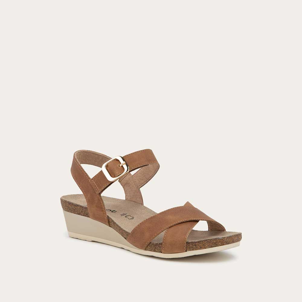 Angled profile  view of a cork footbed, brown wedge sandal with cross straps and a gold buckle on the ankle strap. 
