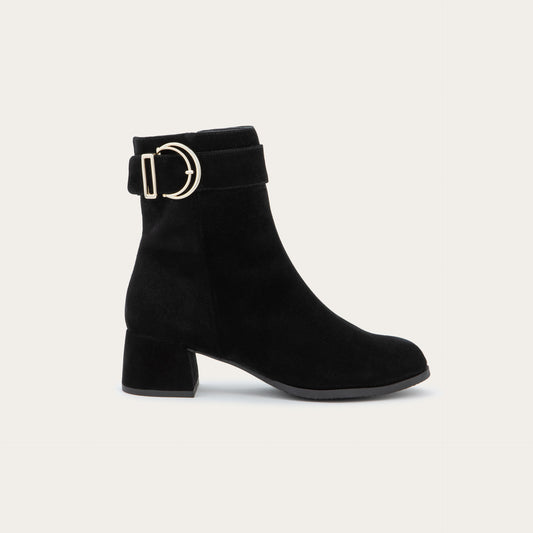 Profile view of a black suede ankle boot featuring a low block heel and a decorative gold-toned buckle strap around the ankle.