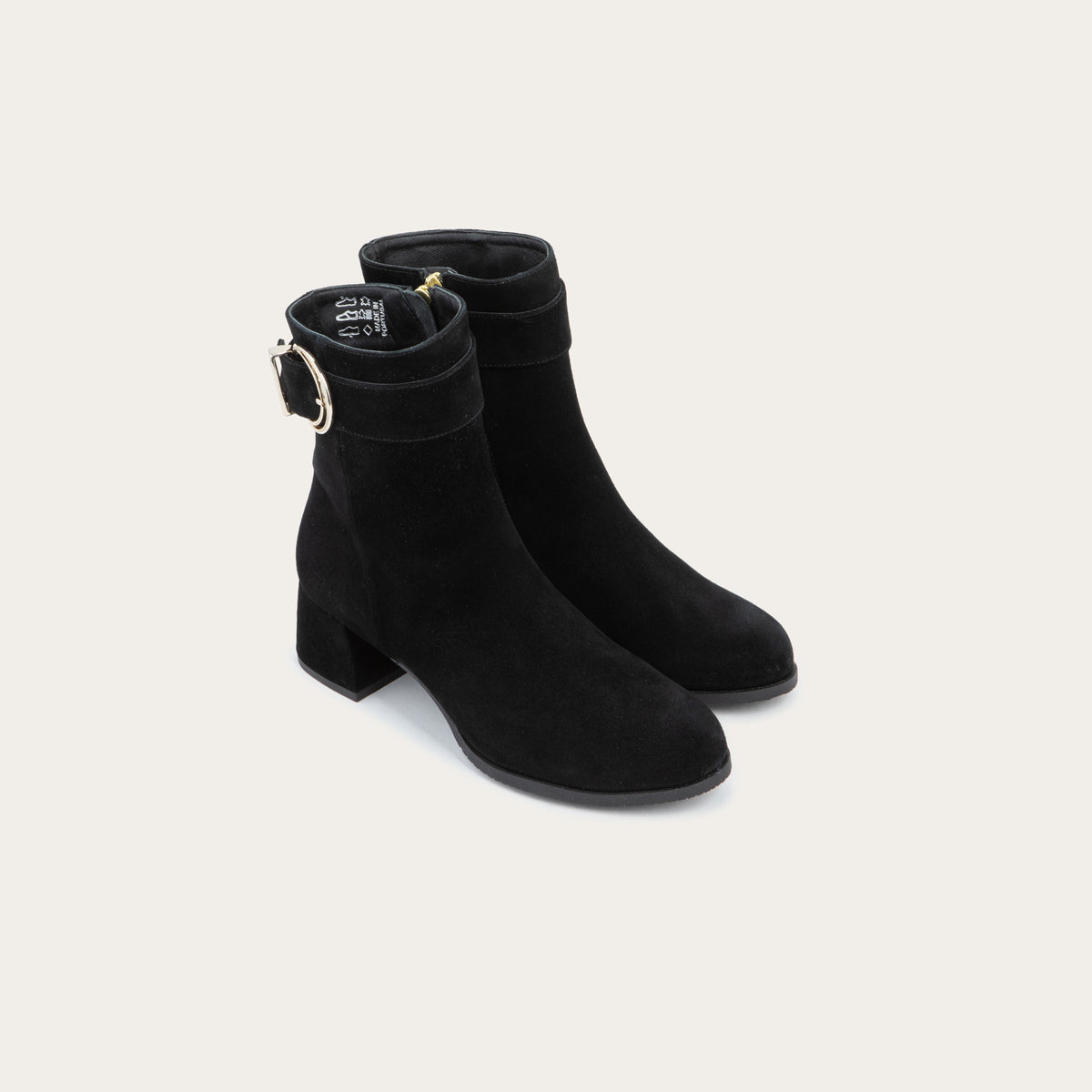 A pair of black suede ankle boots featuring a low block heels and a decorative gold-toned buckle straps around the ankle.