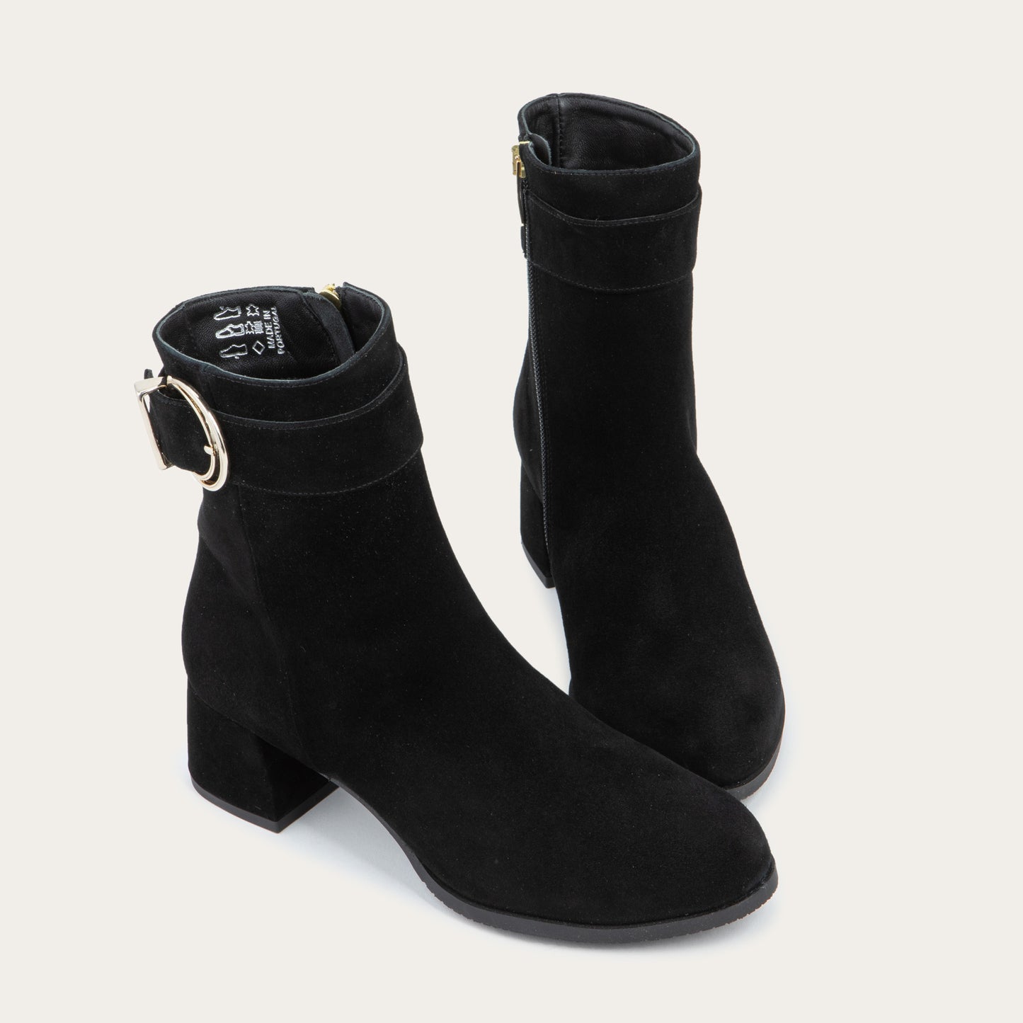 A pair of black suede ankle boots featuring a low block heels and a decorative gold-toned buckle straps around the ankle.
