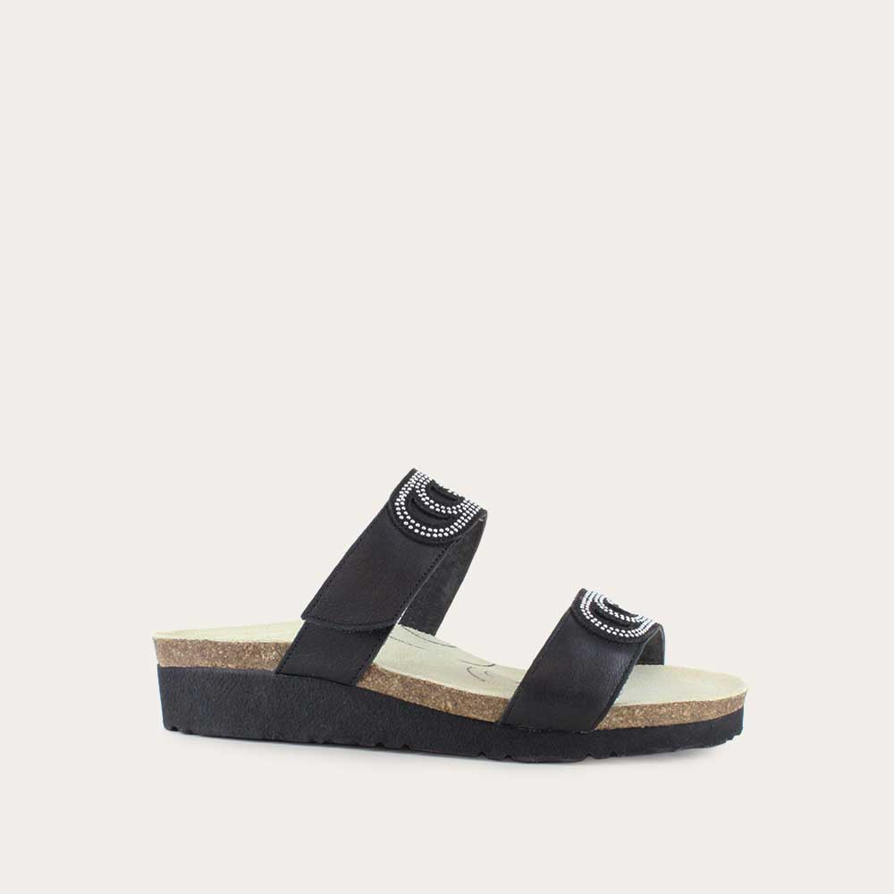Angled profile view of a black leather slip on wedge sandal with two straps and reivet detailing on a cork footbed,