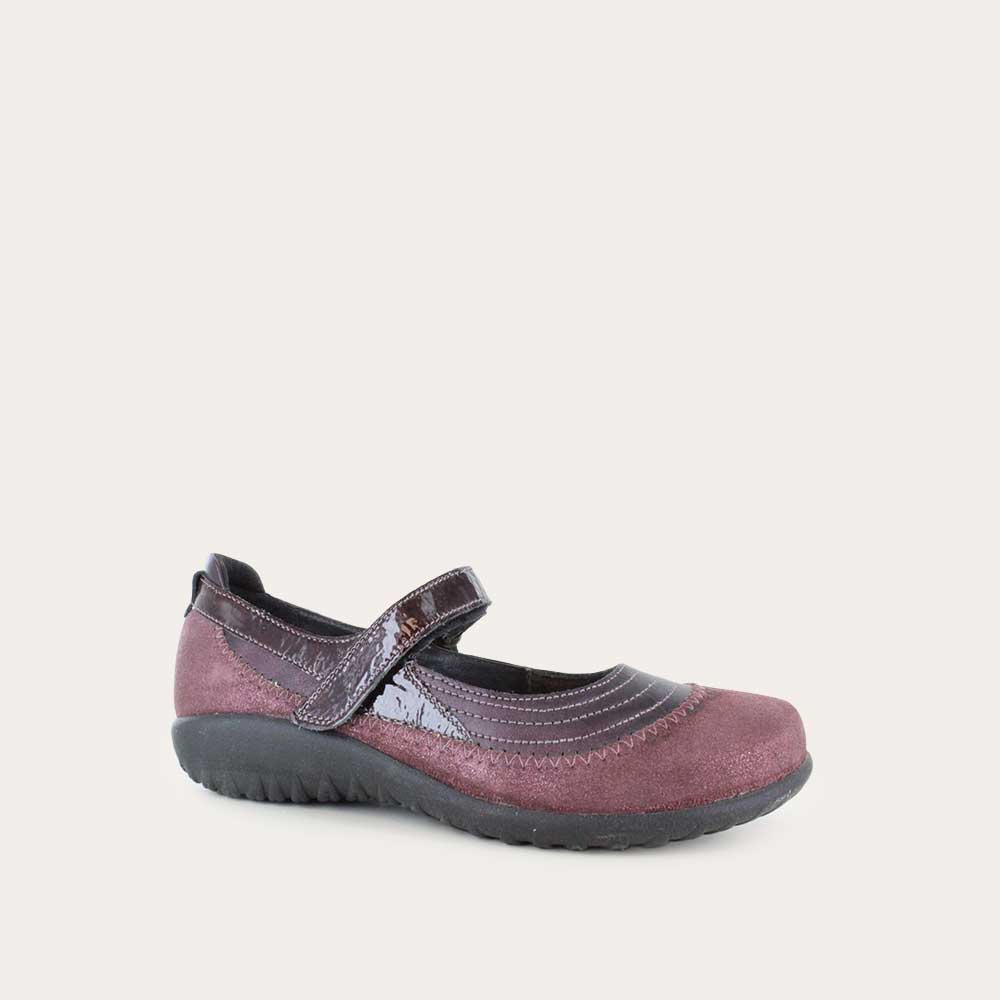 Angled profile view of a purple mary jane featuring contrasing shimmer suede and shiny leather on a black sole.
